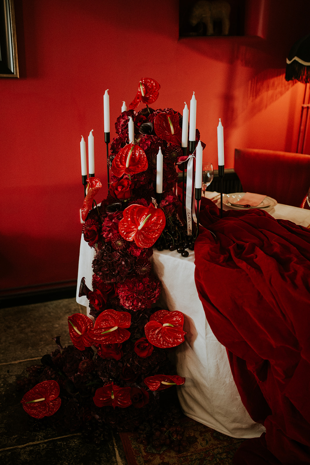 detail shot of Anthurium trailing from a wedding breakfast table with candles within. A stunning display for a cherry red winter wedding