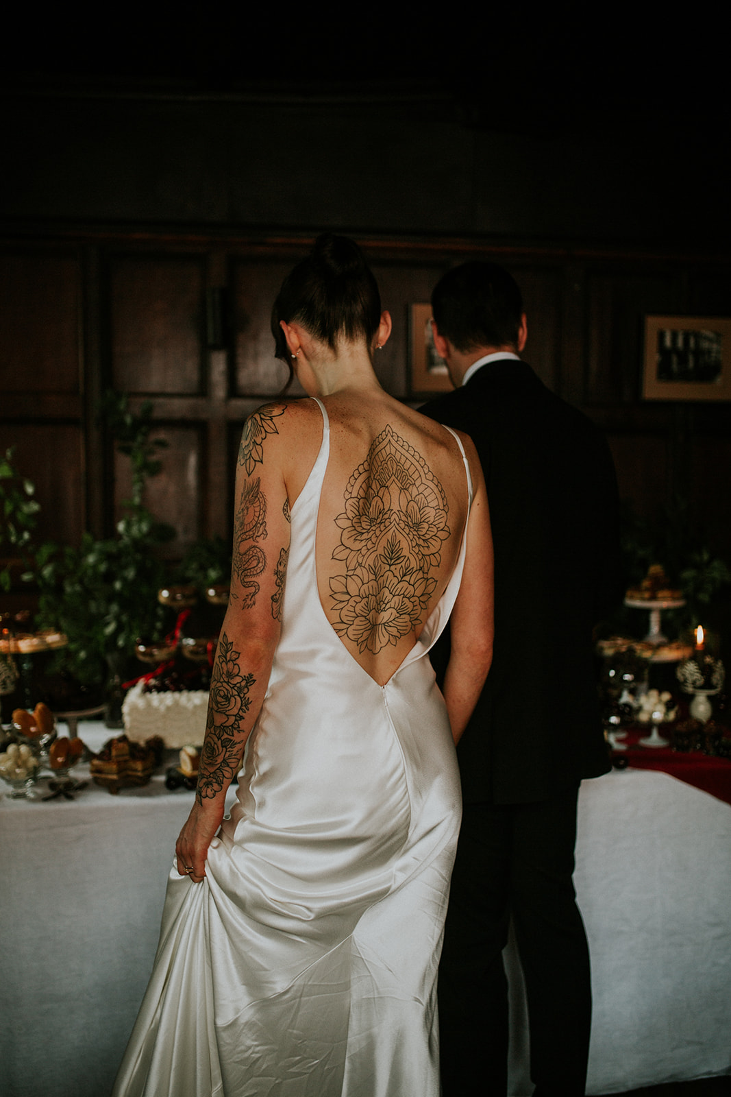 detail shot of the back of the bride who wears a deep plunging backless dress which shows her tattooed back and arms