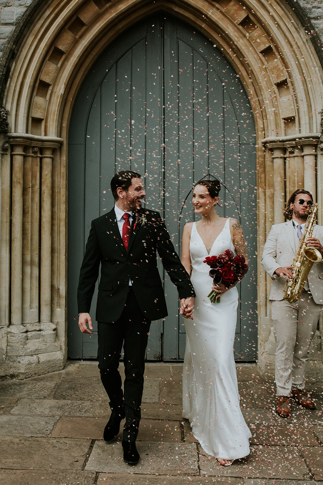 bride and groom leaving the church with a saxophonist playing in the background. They walk through confetti
