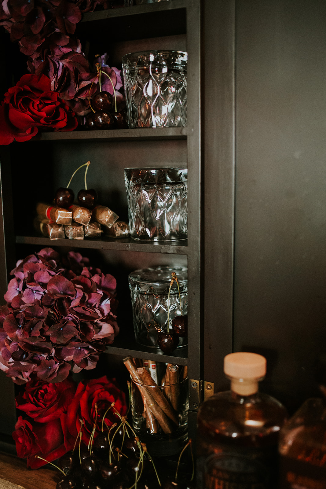 detail shot of a whisky and cigar bar with deep red wedding flowers