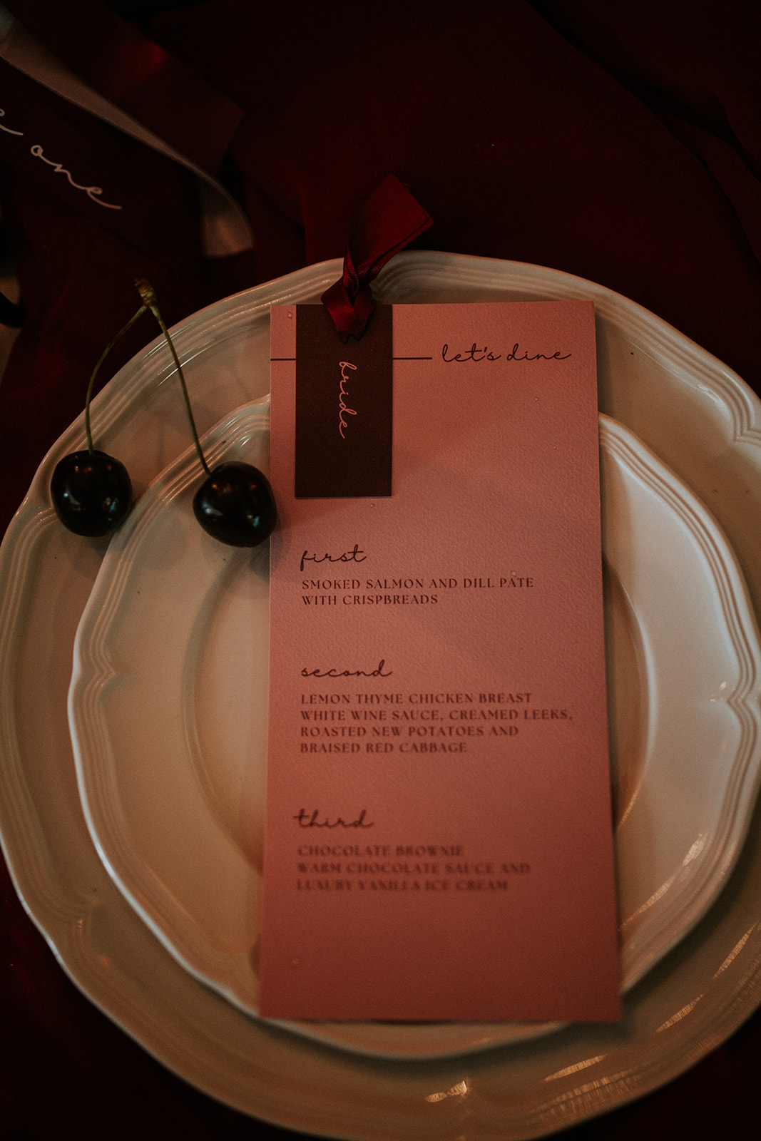 detail shot of bride place setting with pink menu and cherries on white wedding china