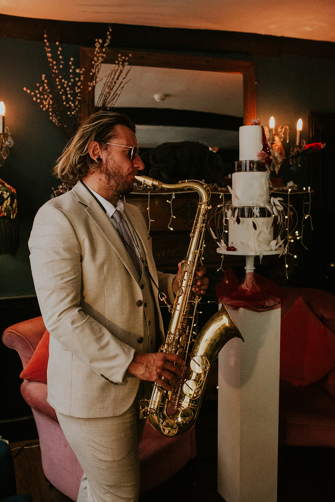wedding saxophonist playing inside of the wedding venue with a sculptural wedding cake in the background