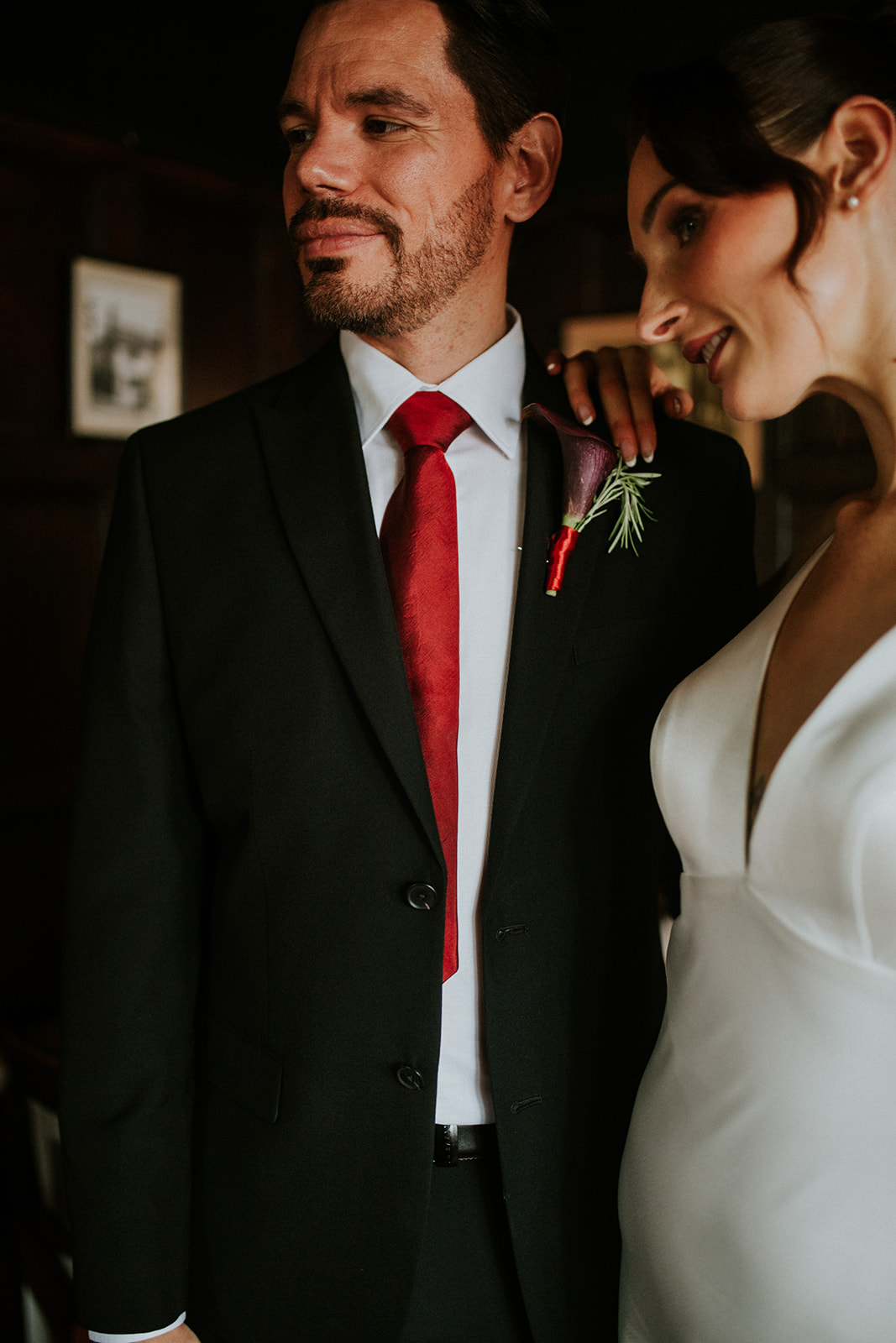 detail shot of groom wearing black two piece suit with white shirt and red tie for cherry red winter wedding