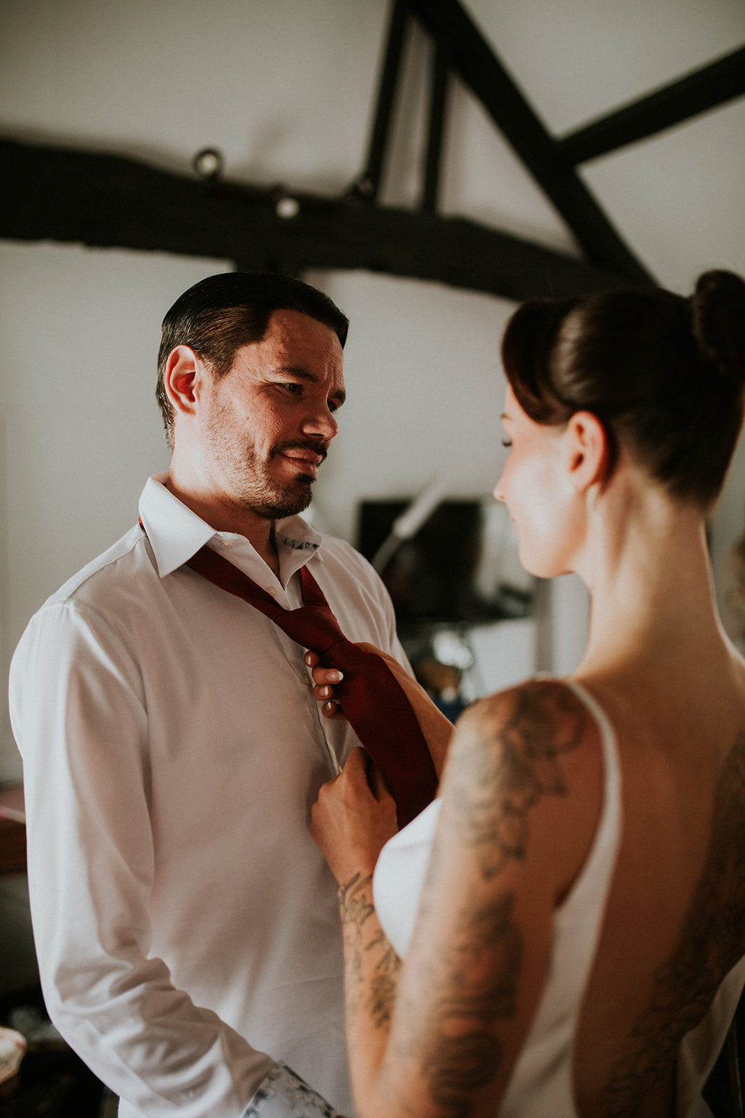 bride hels groom do his tie up on the morning of their cherry red winter wedding
