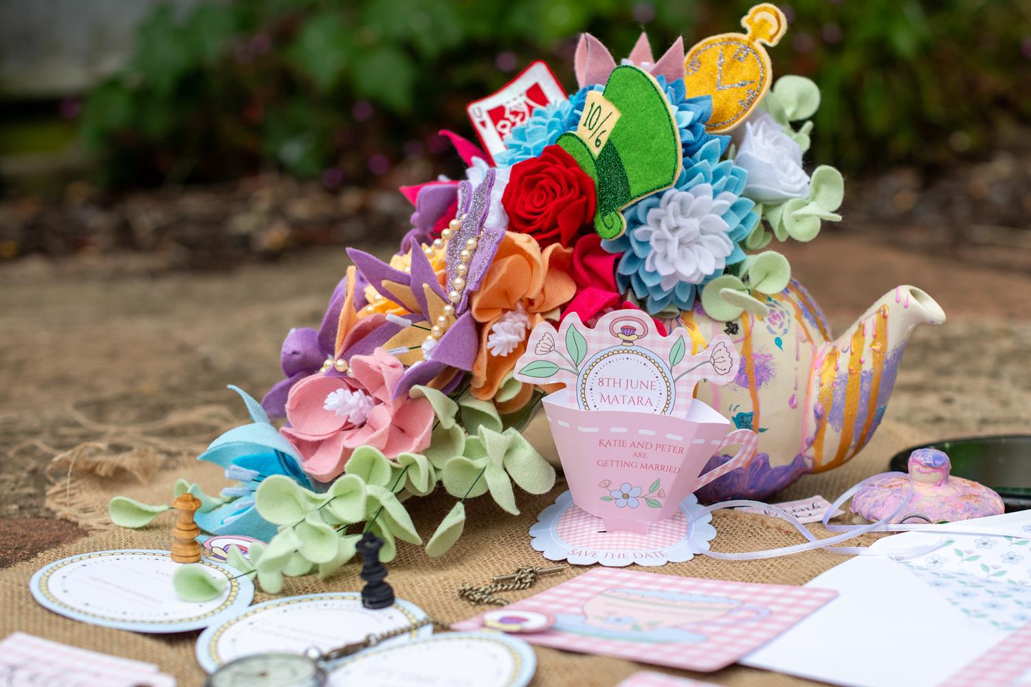 Boom Bridal colourful cascade wedding bouquet - alice in wonderland themed bouquet - colourful felt flowers flow out of a tea pot on a wedding table