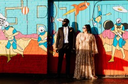 engaged couple stand in front of a graffiti wall wearing sunglasses