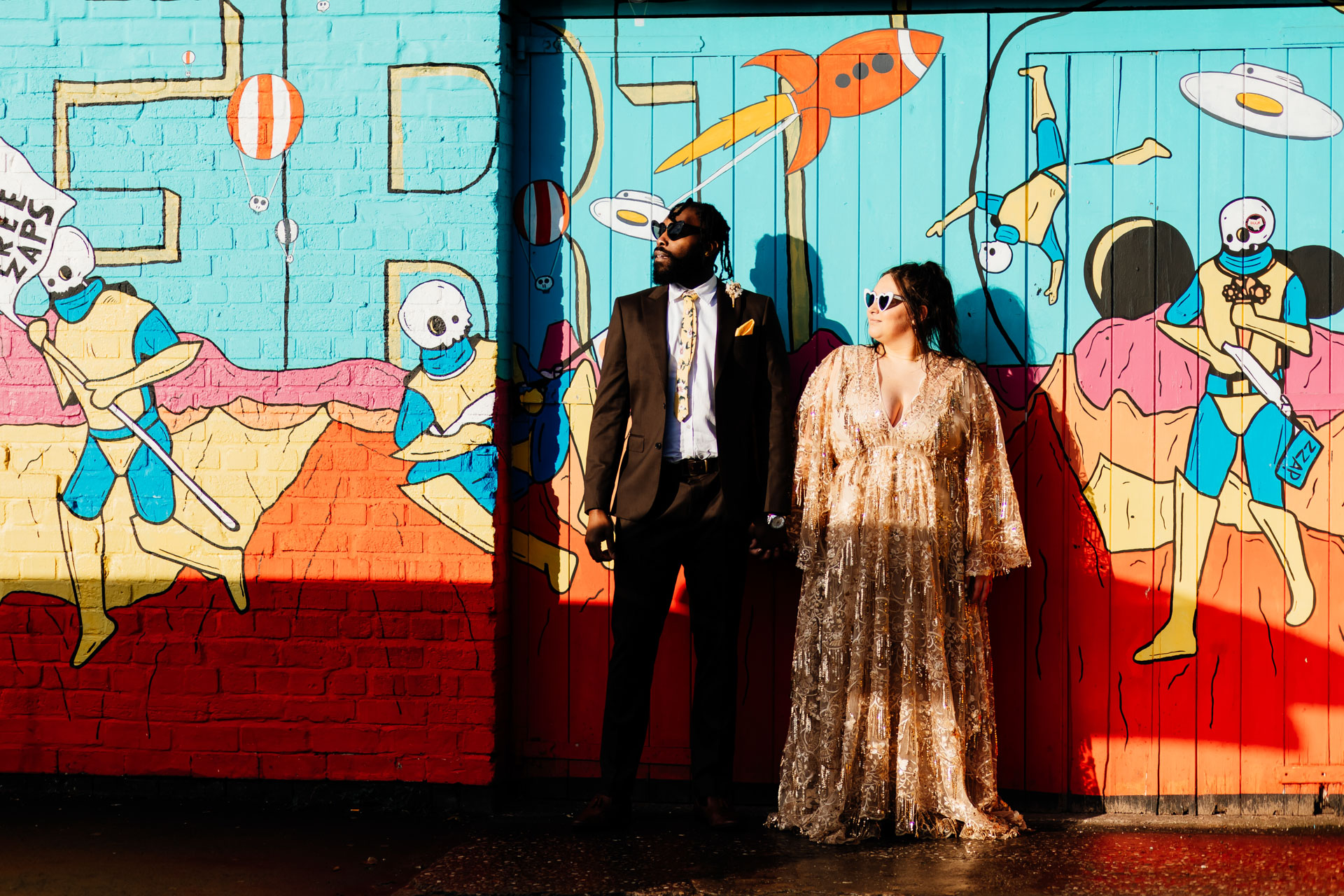engaged couple stand in front of a graffiti wall wearing sunglasses