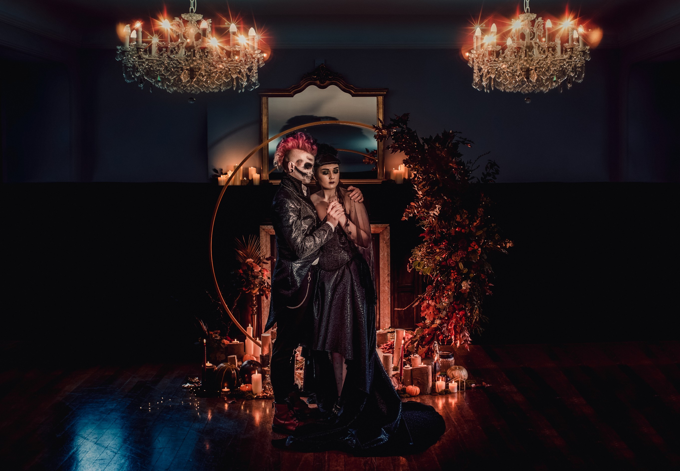 Gothic halloween wedding couple in the candlelight lit by two dramatic chandeliers against a dramatic floral arch backdrop at abbot oak wedding venue