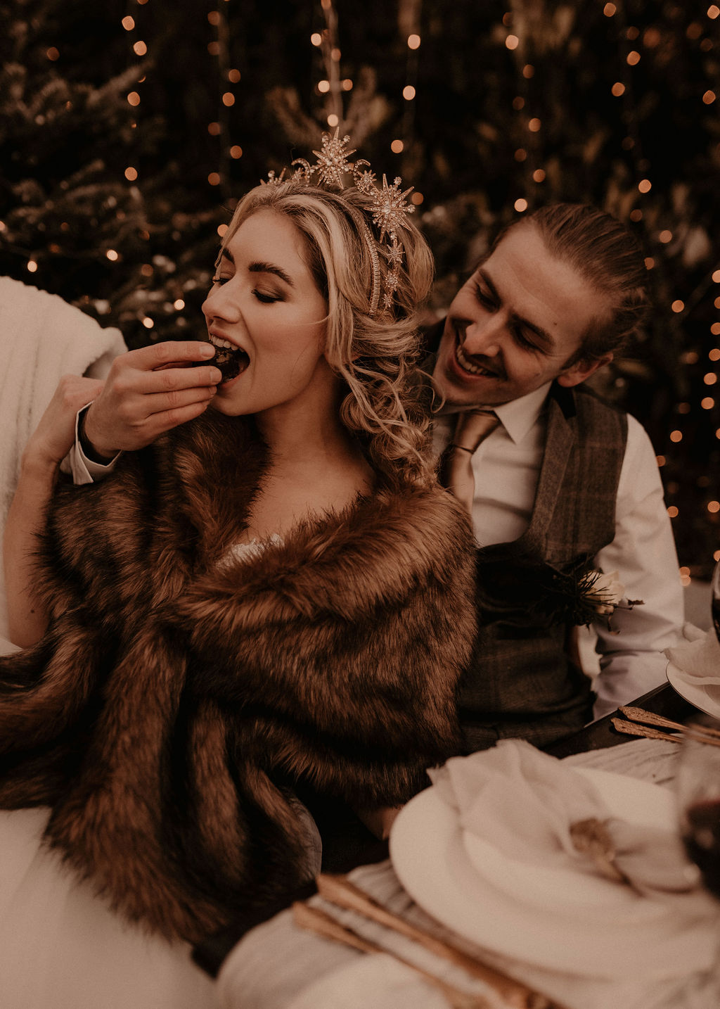 Elegant winter wedding inspiration in the snow - elopement wedding - couple feeding each other cake with fur throws and sparkley lights