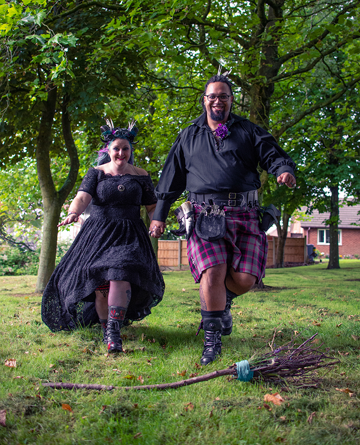 bride and groom jumping the broom - gothic garden wedding - black wedding dress - gothic groom wearing kilt - alternative wedding ceremony