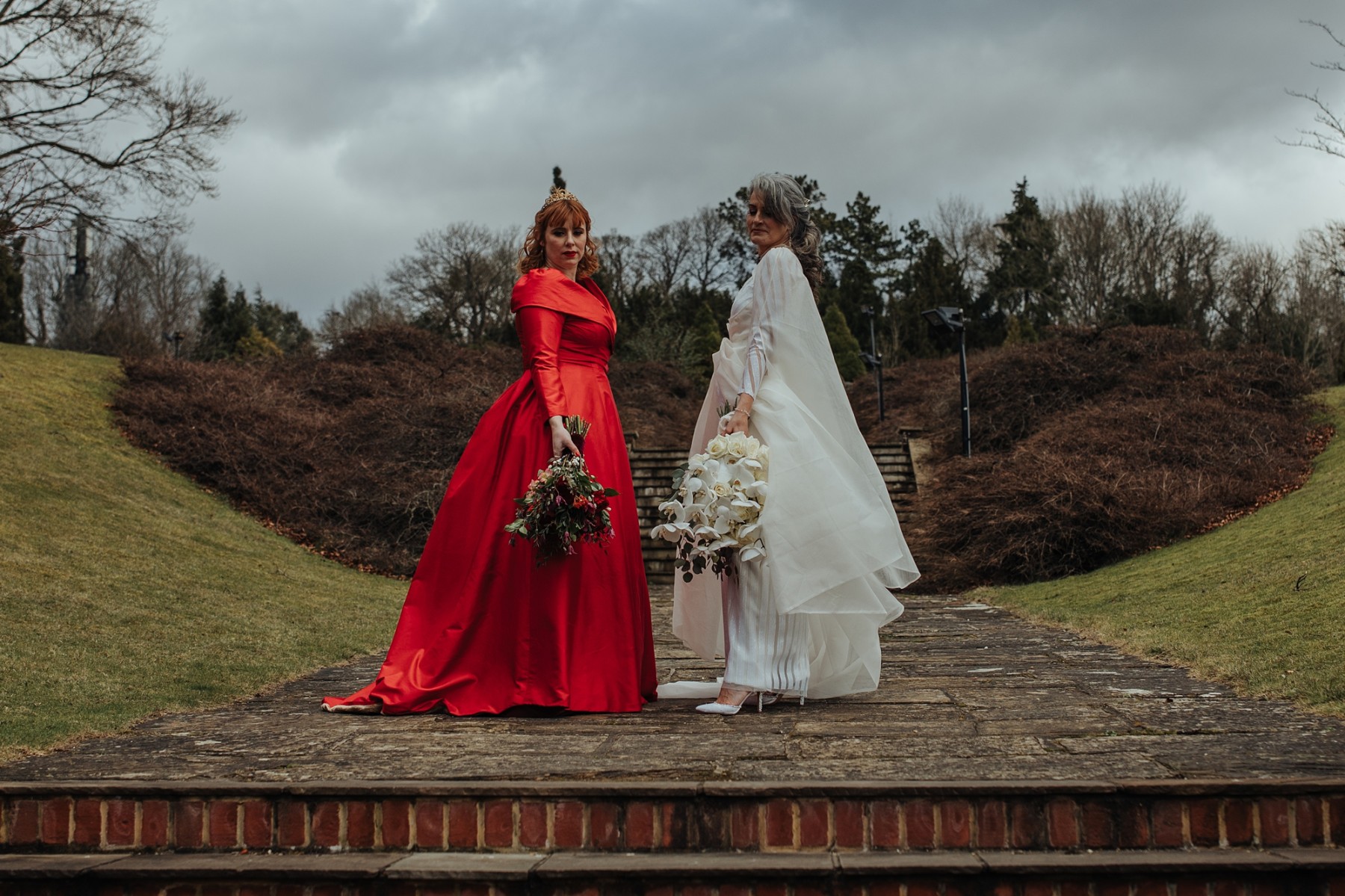 two brides, one in a red wedding dress and one in a white wedding dress - unique bespoke wedding dresses - regal wedding dresses