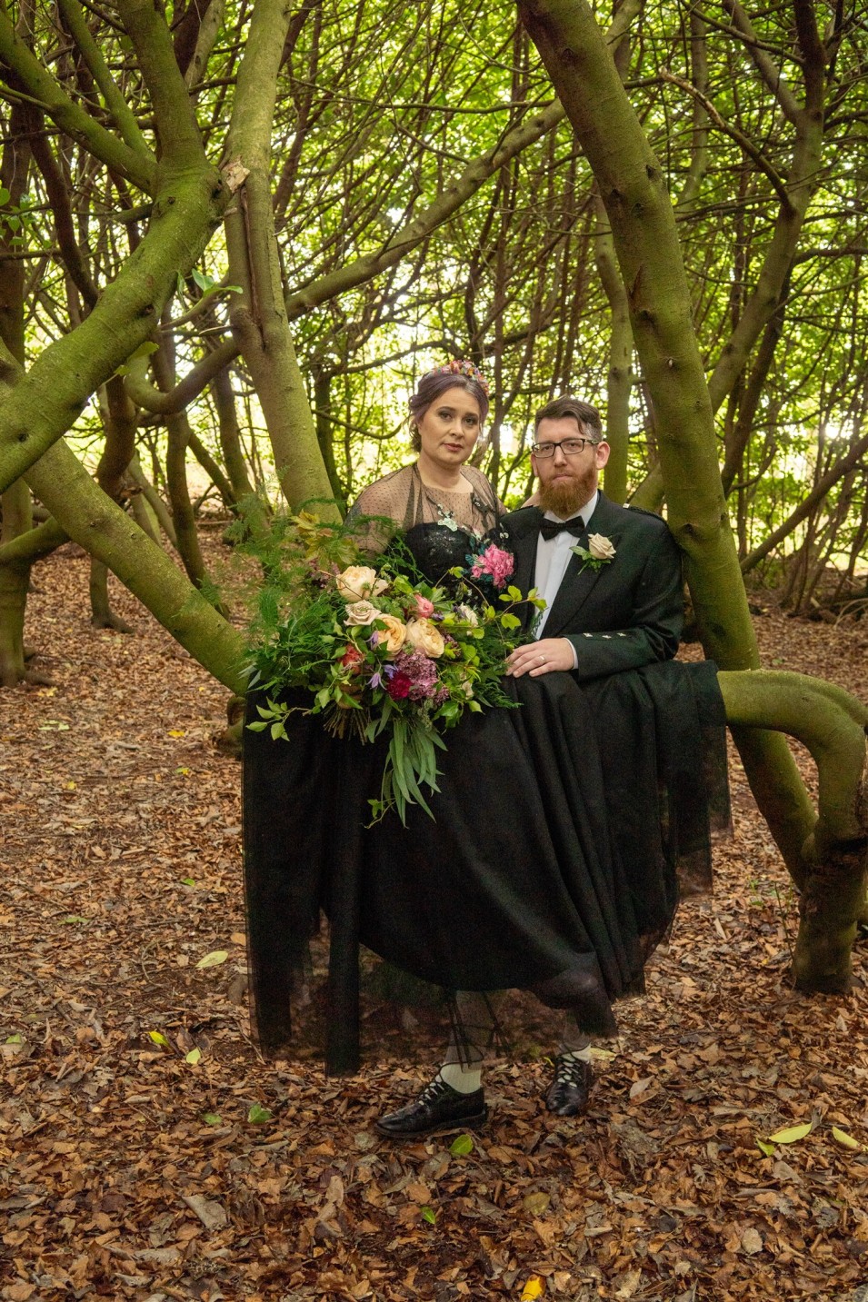 ethereal woodland wedding - bride and groom sitting in a tree dressed in black