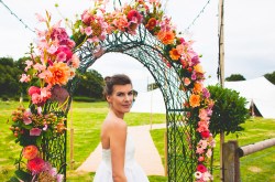 Bride Stood Under Colourful Floral Archway - Worcestershire Wedding Florist - Locally Grown Ceremony Table Flowers - Wedding Flowers - Wild Country Wedding Florist - Unconventional Wedding - Flowers From The Farm Worcestershire - Georgia's Flowers
