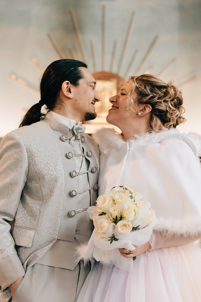 bride wearing handmade white cape and groom in prince charming style suit