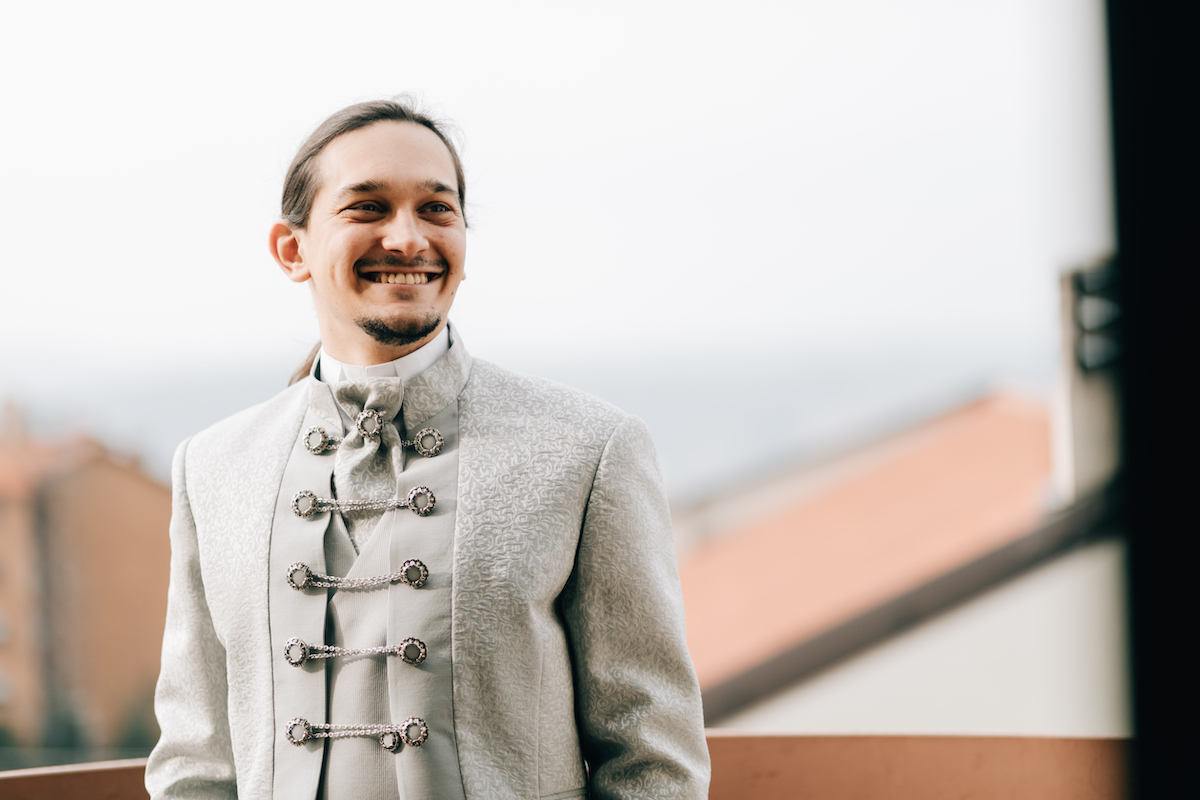 long haired groom wearing prince charming style wedding suit with silver buttons and chains