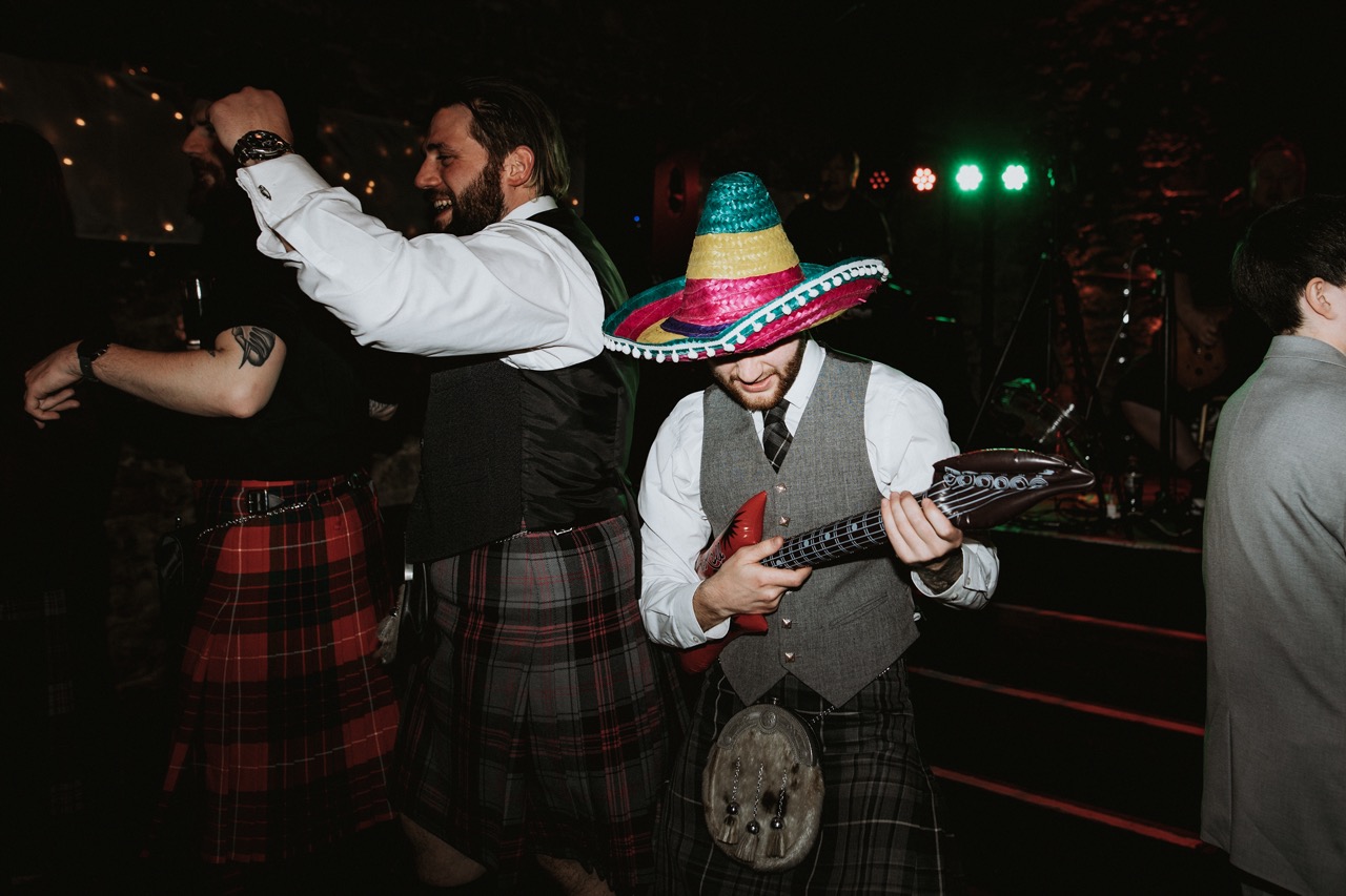 wedding guest wearing a sombrero and playing an inflatable guitar on the dance floor