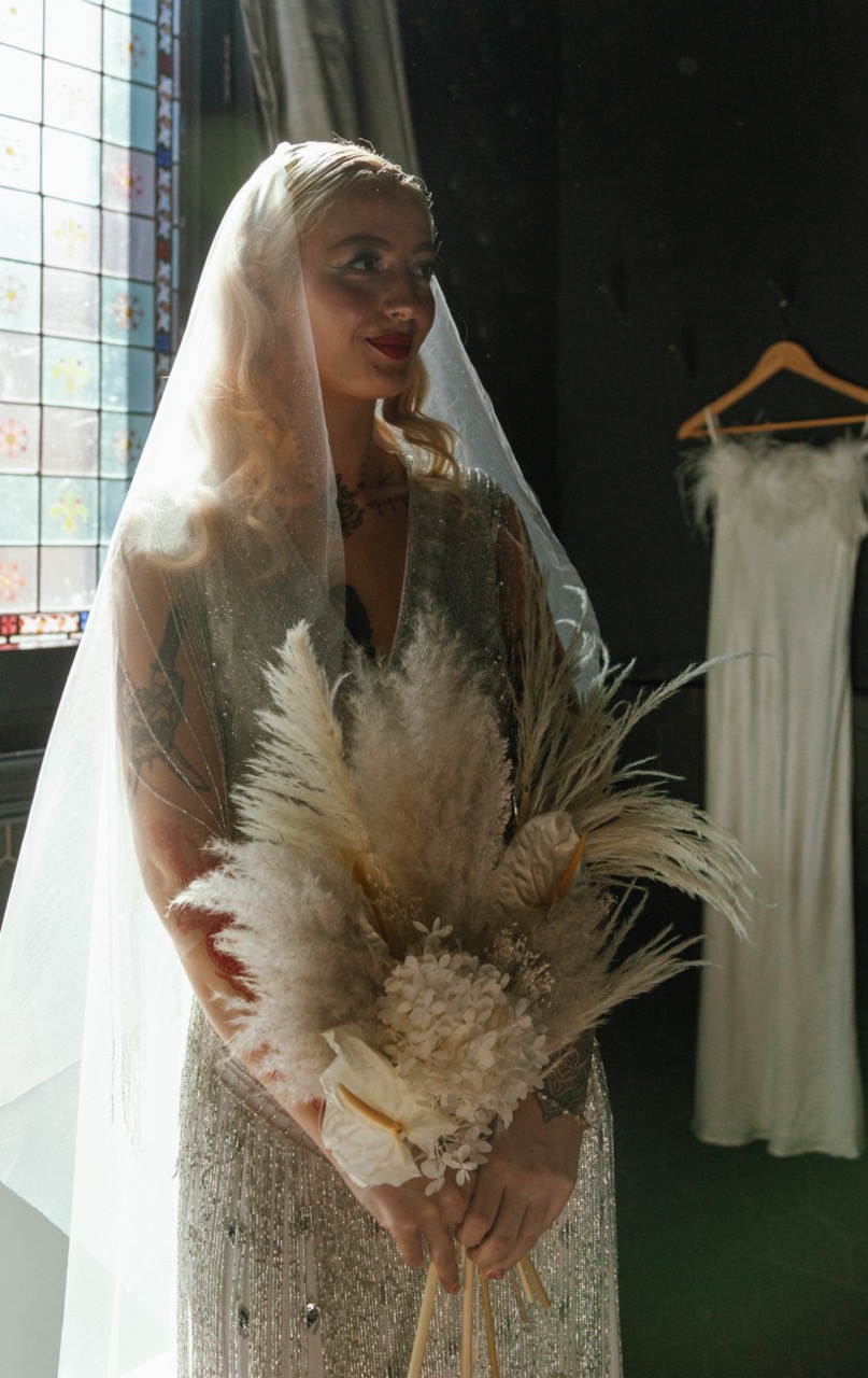 bride with sheer veil and dried flower bouquet, backlit by church window
