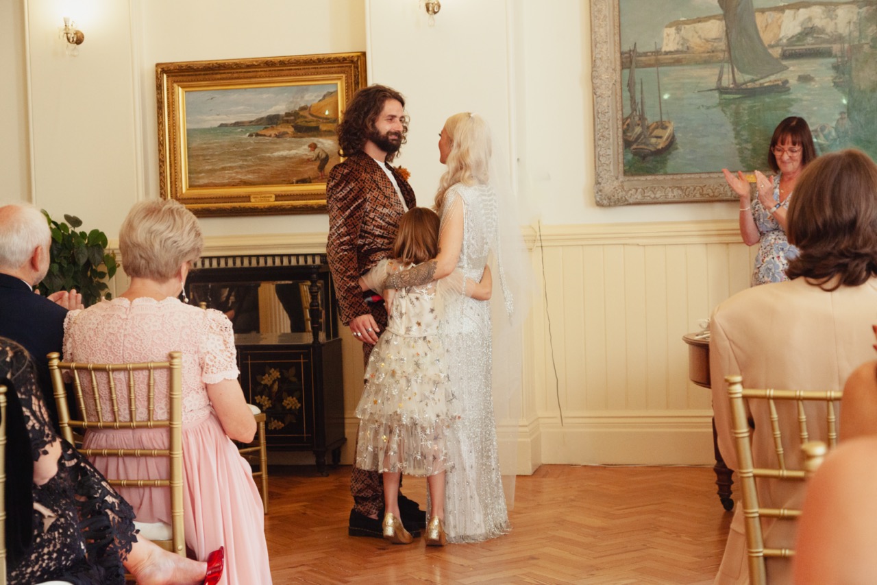 family hug at wedding ceremony in brighton - bride and groom embracing their daughter