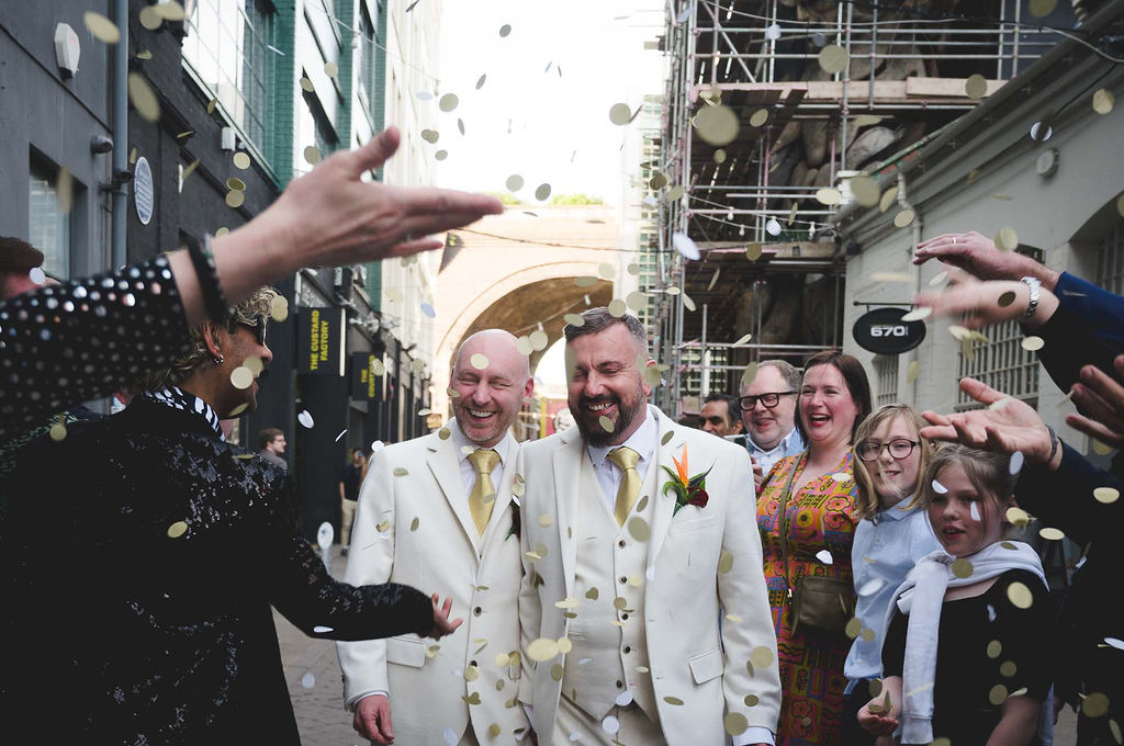 two grooms smiling as confetti is thrown over them