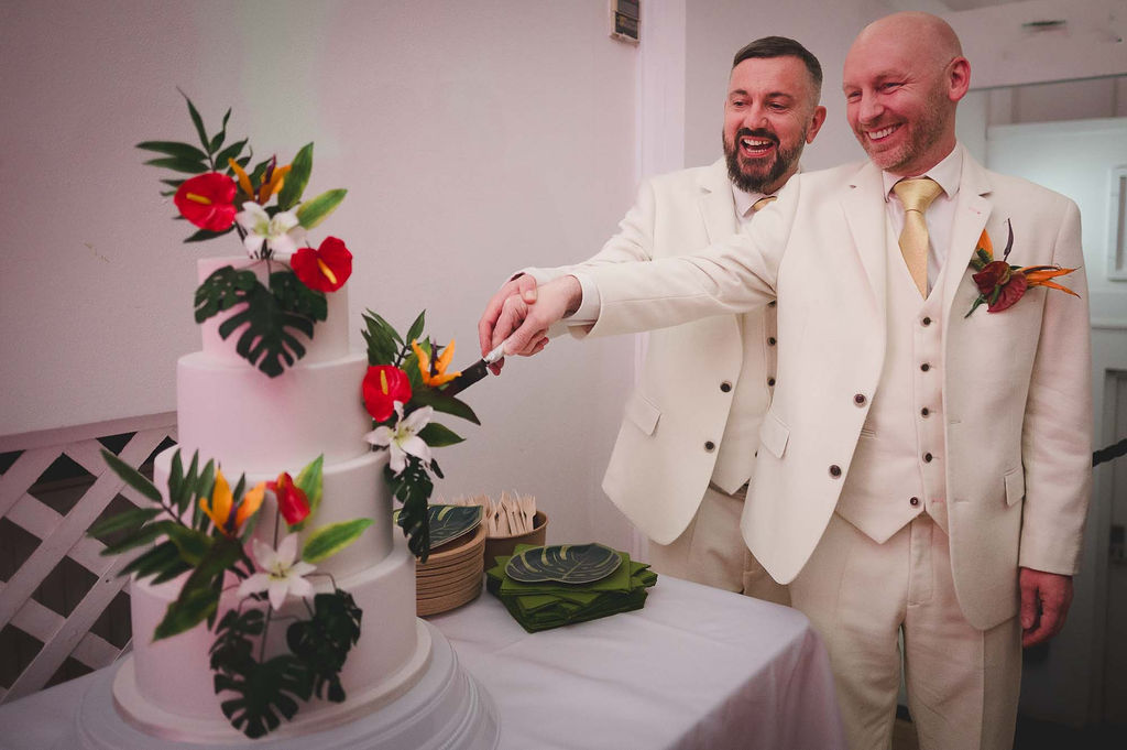 two grooms cutting their tropical themed wedding cake