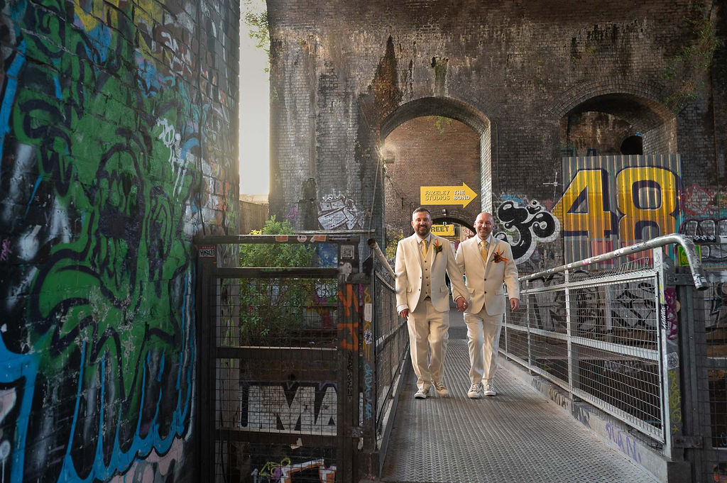 two grooms in ivory suits walking through Digbeth in Birmingham