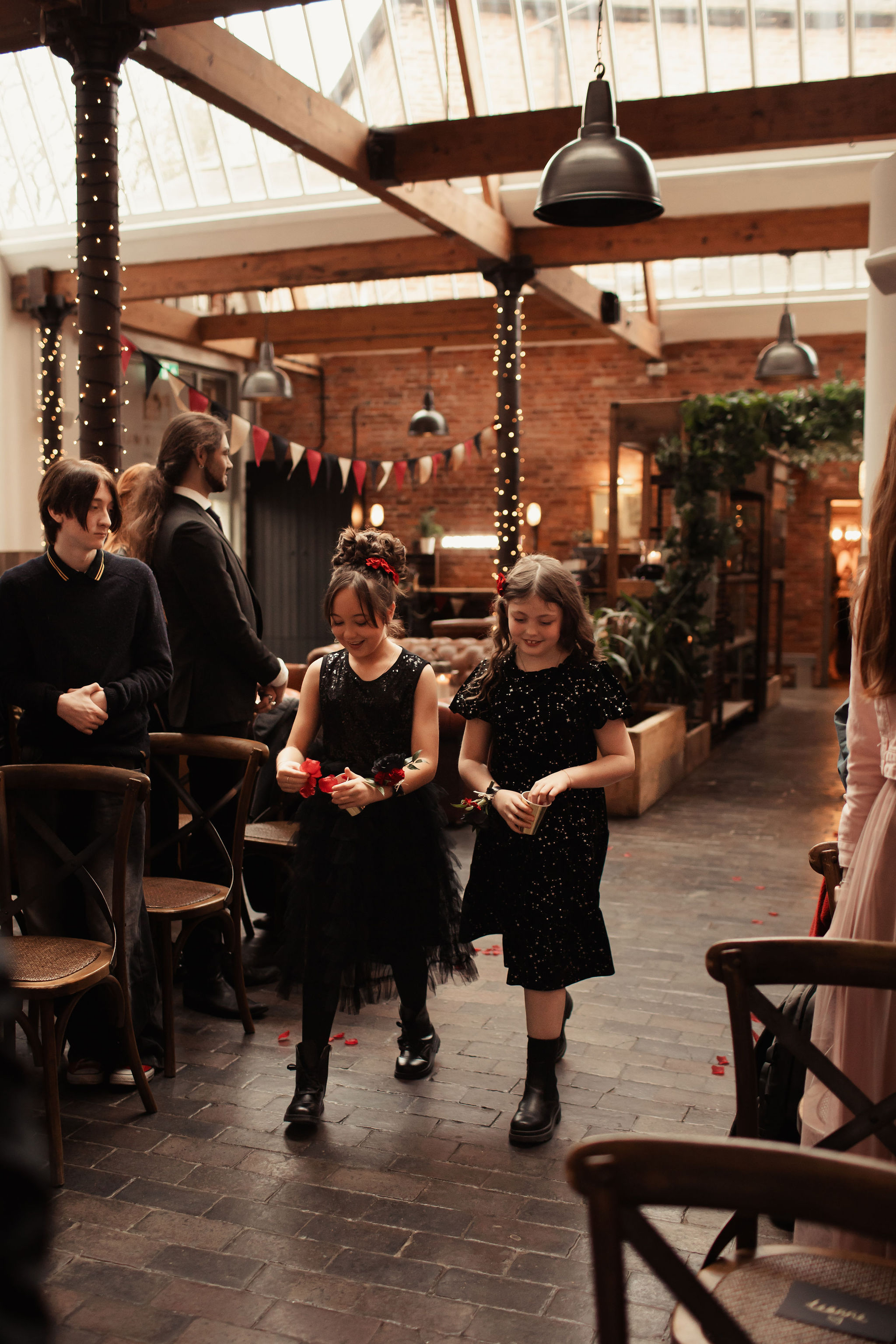 bridesmaids in black dresses scattering petals down the aisle
