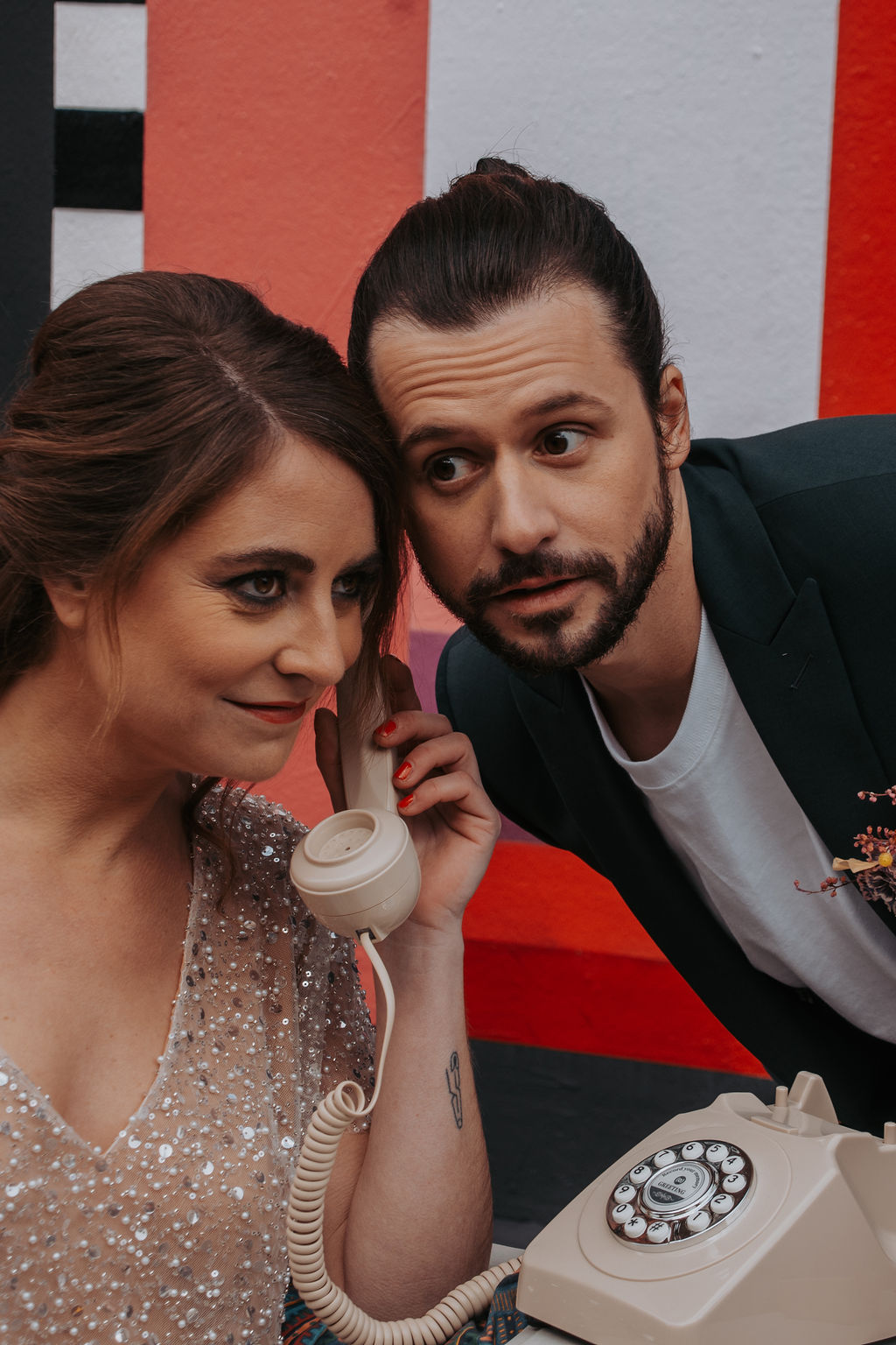 alternative bride and groom stand in front of a graffiti wall and play with a old fashioned telephone
