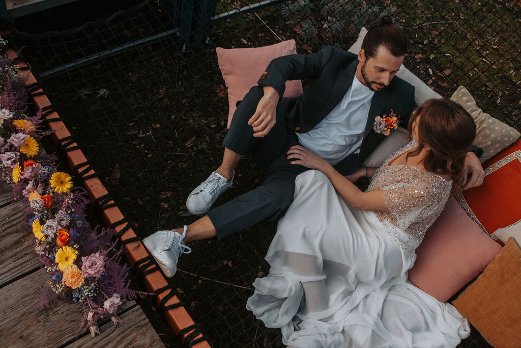 bride and groom wear casual wedding attire and lay on some scatter cushions in a french park