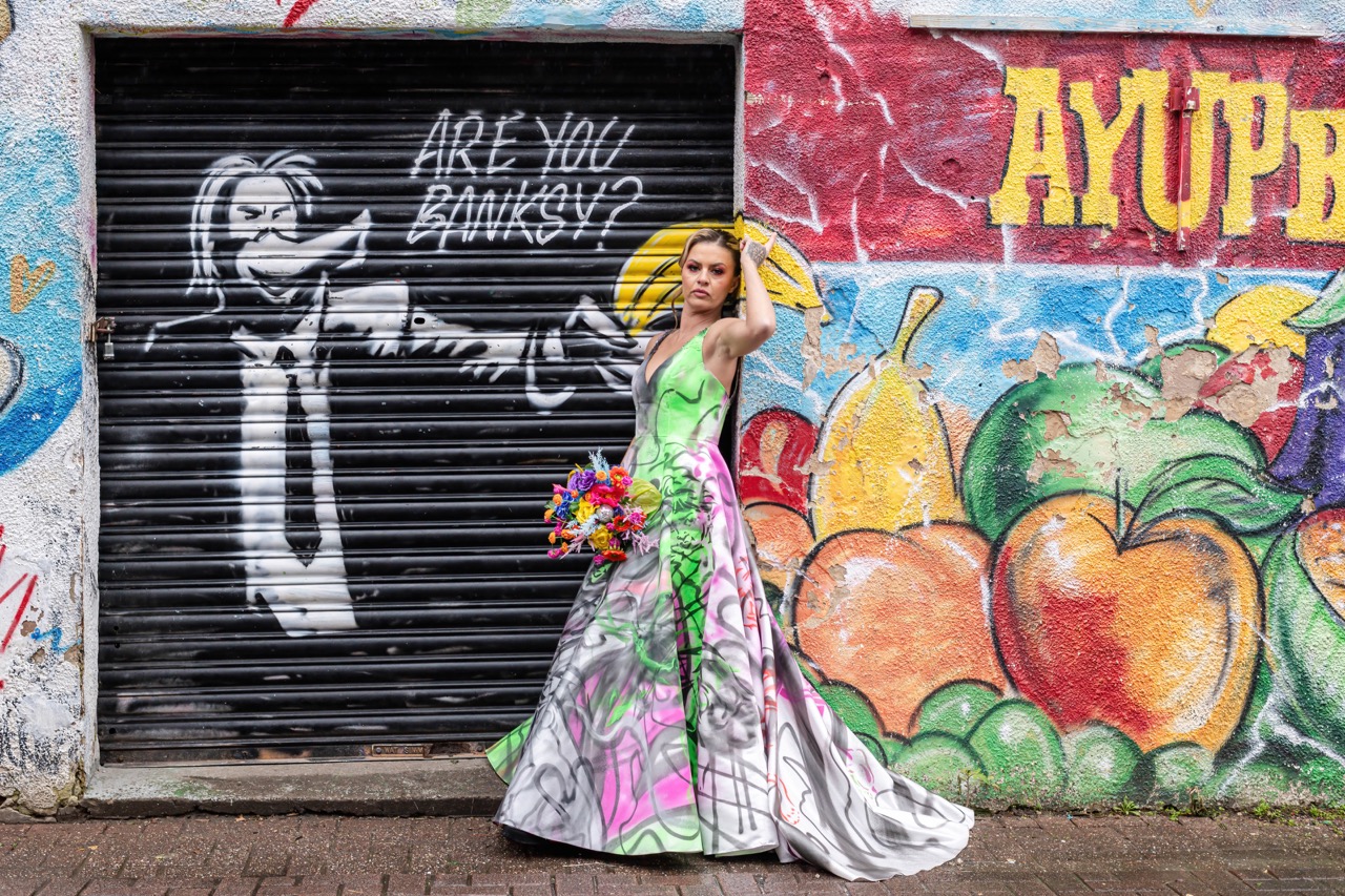 bride wears a colourful art inspired patterned wedding dress and stands in front of an art graffiti wall