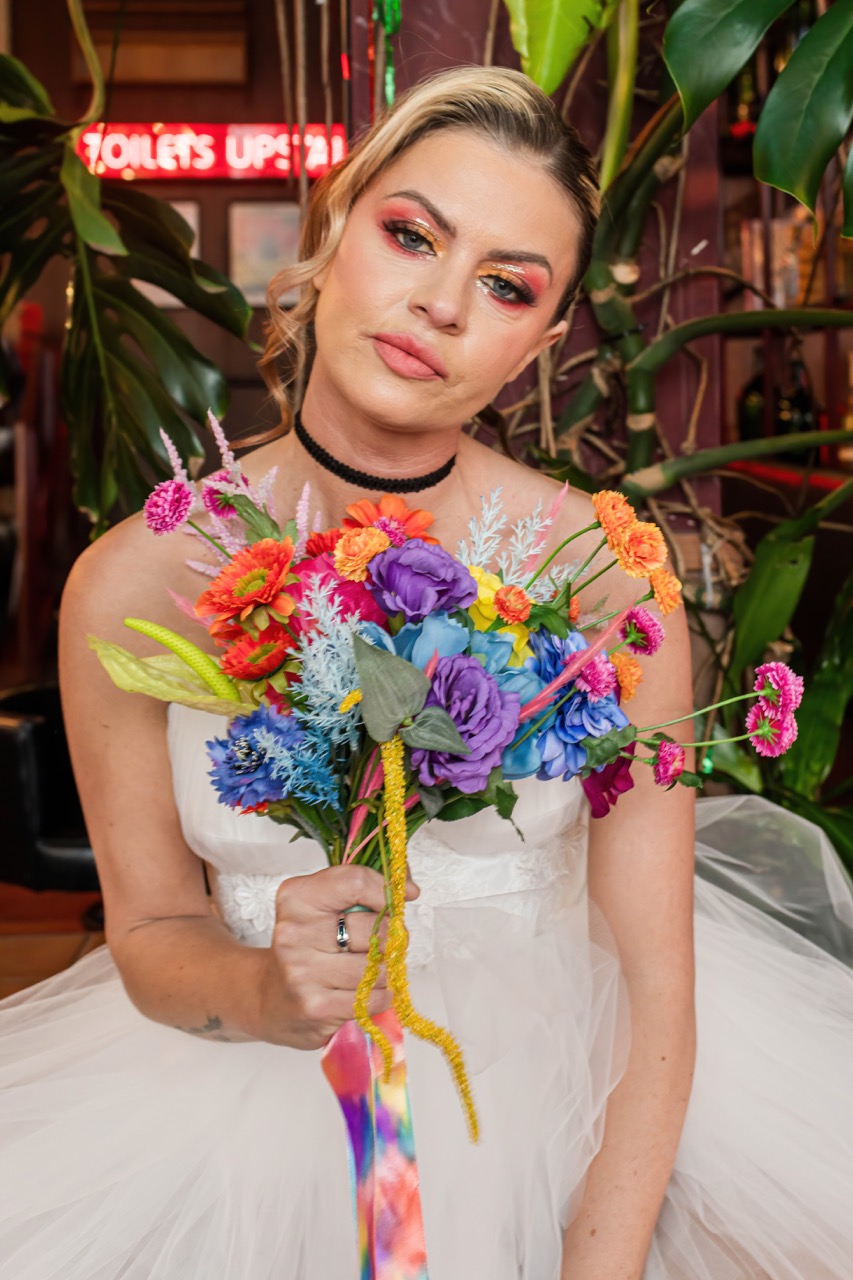 bride sits by large indoor house plant and holds her multicoloured bridal bouquet