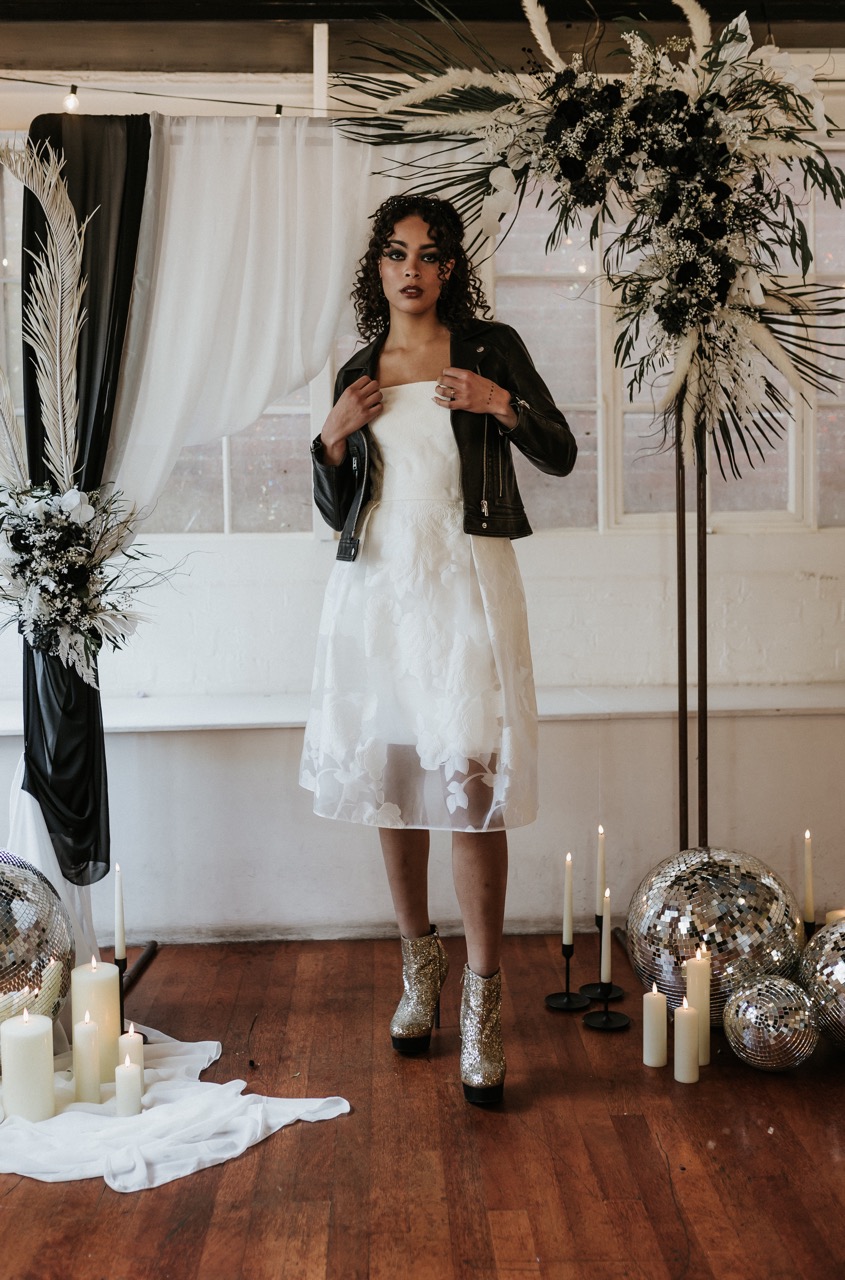 bride wearing knee length wedding dress with black leather jacket and sparkly boots