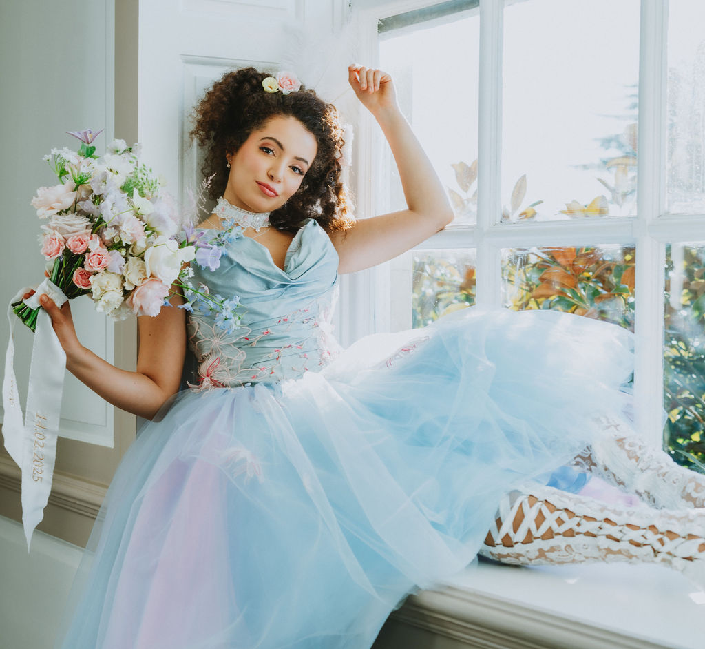 bride sat on window sill wearing pastel blue wedding dress