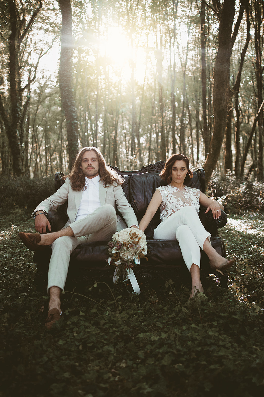bride and groom sitting on black sofa in the forest