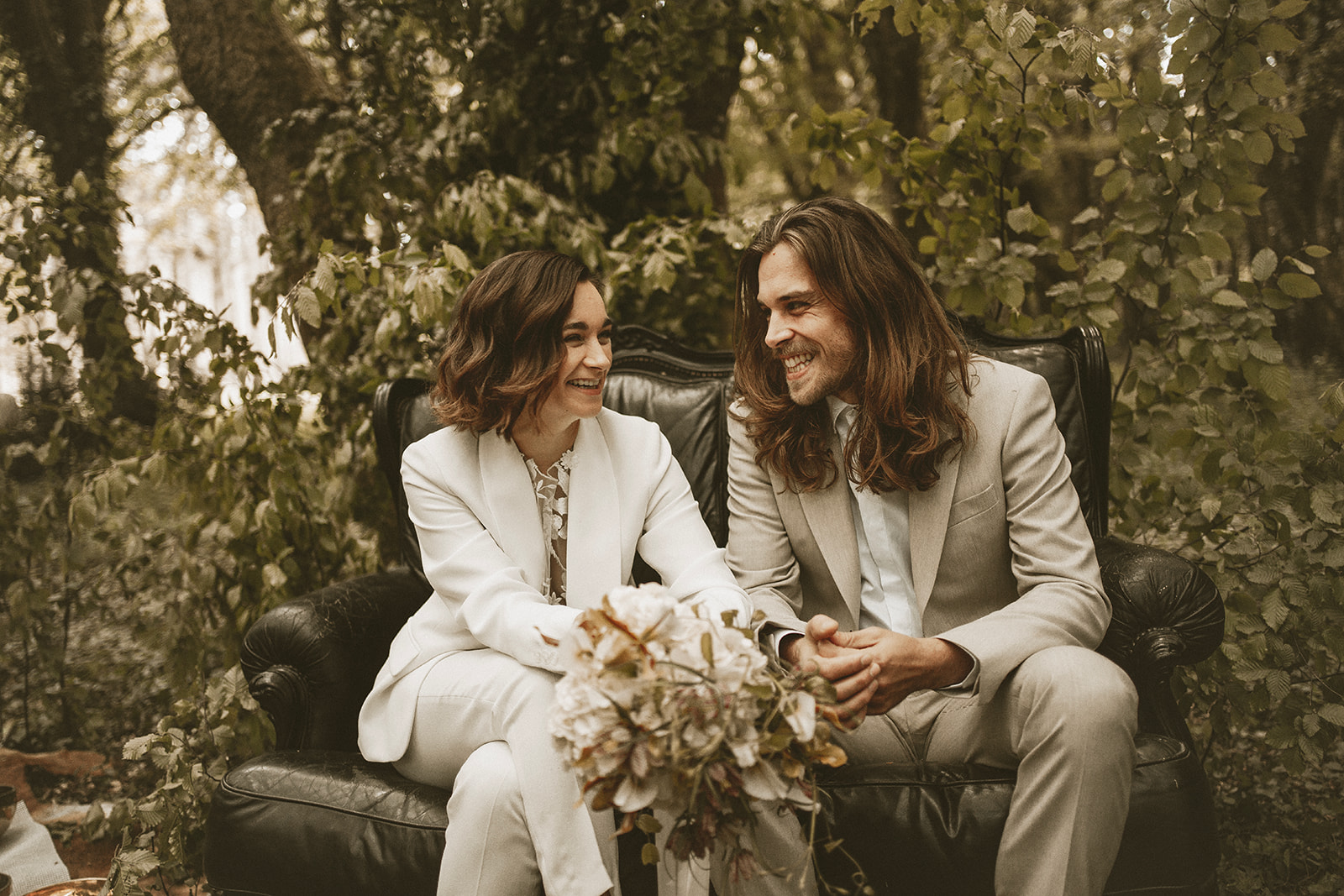 bride and groom sitting on a sofa in the woods for their woodland wedding ceremony