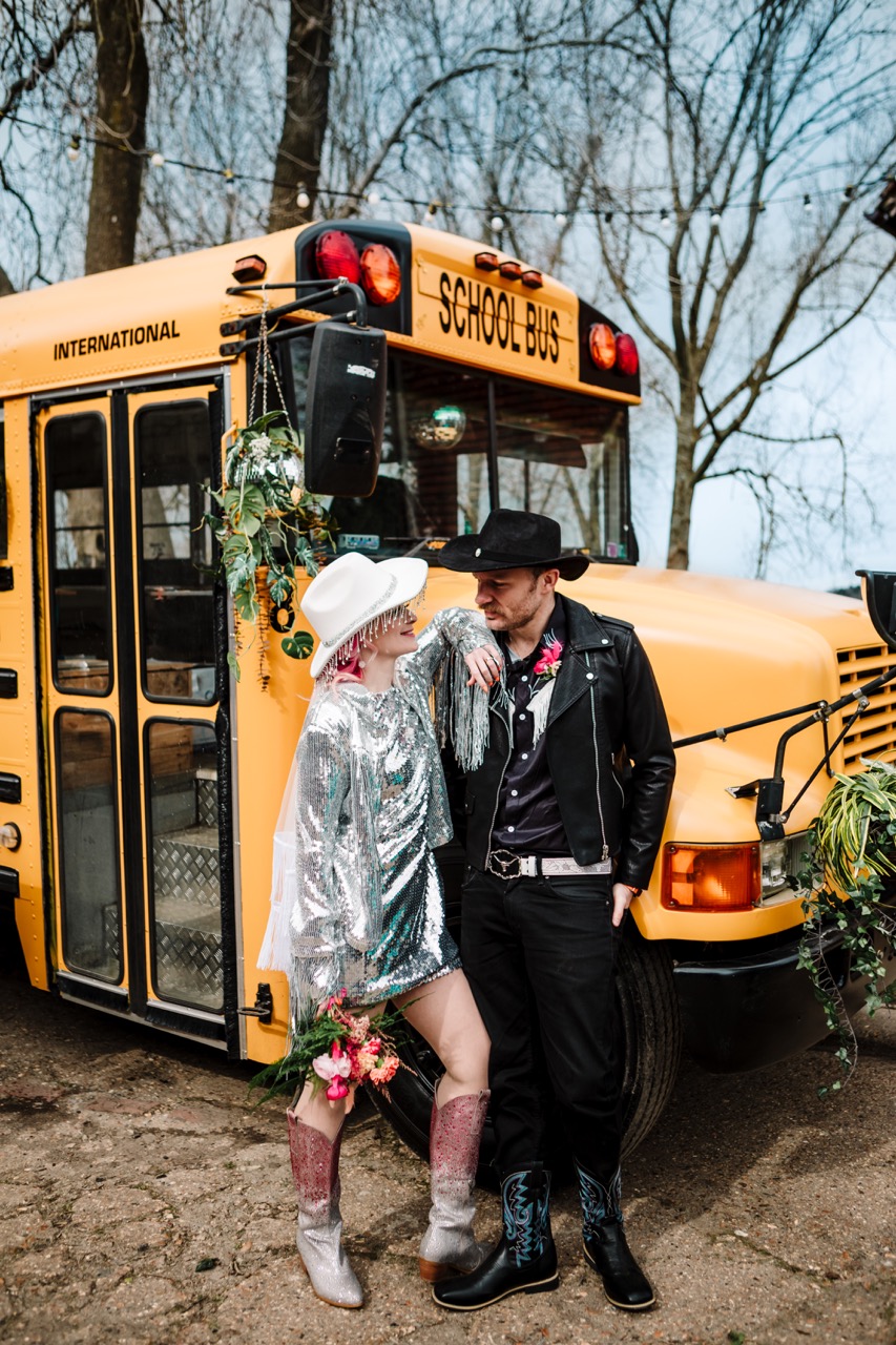 bride and groom in cowboy hats standing infront of american school bus