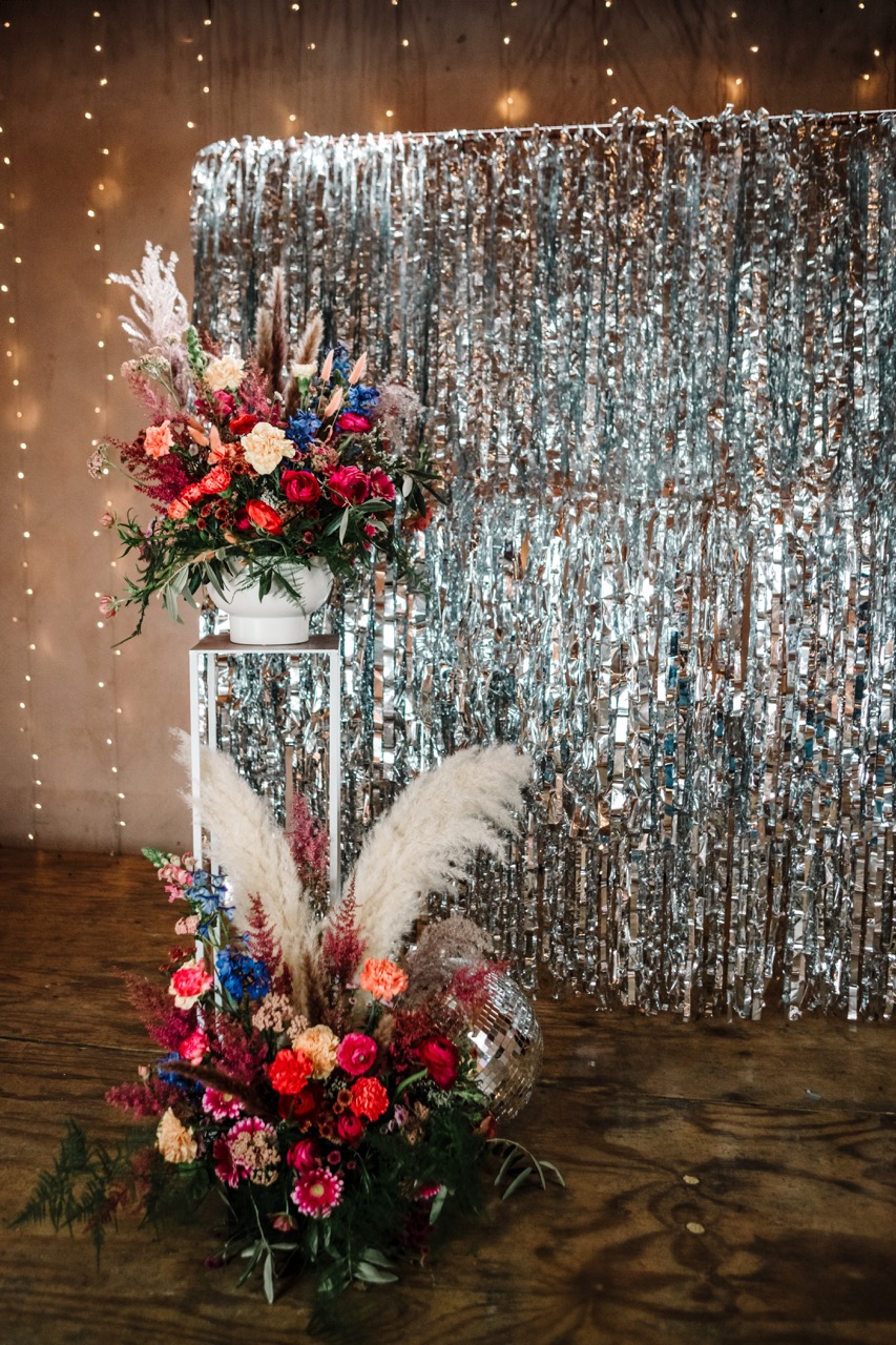 silver tassle wedding backdrop with colourful wedding flower display