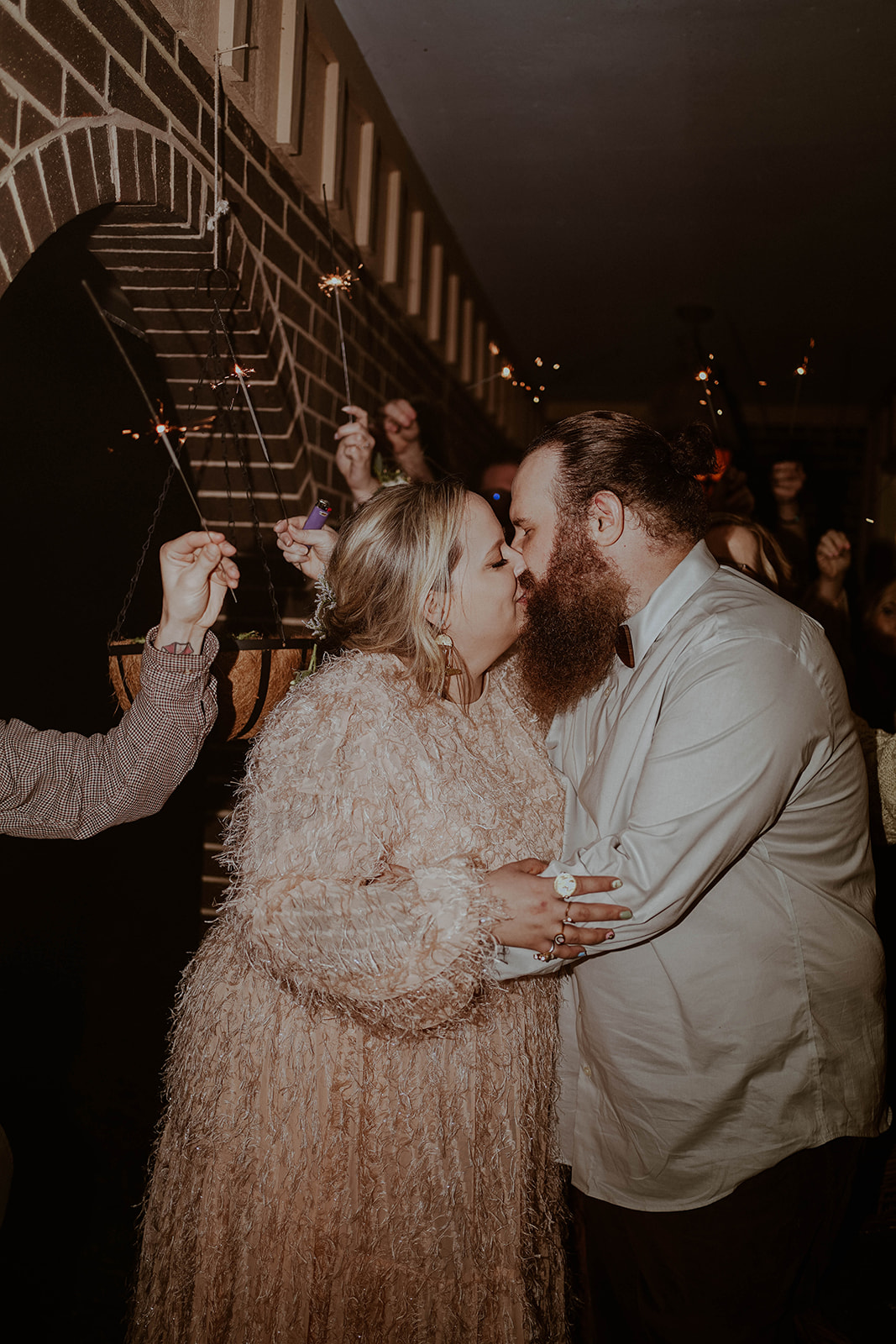 bride and groom kiss as wedding guests hold sparklers