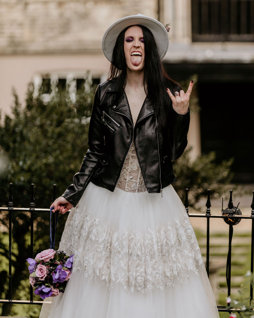 bride wearing a fedora with her tongue out, doing a rock sign with her hand