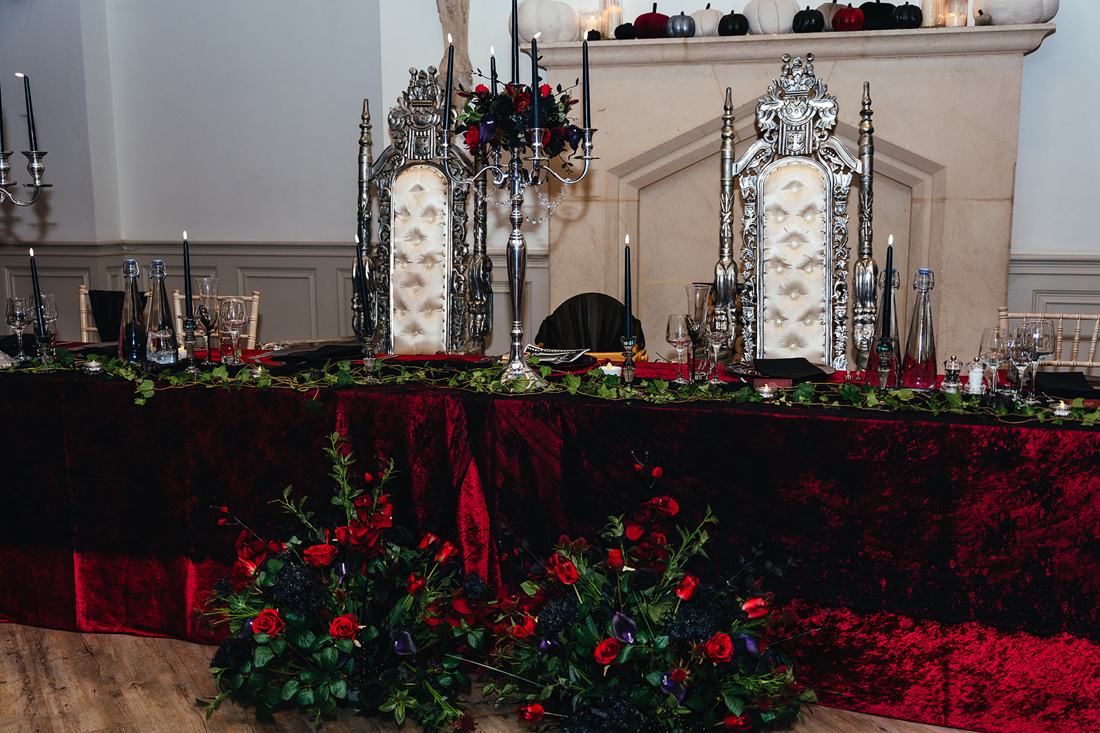 Sweetheart table set up for a gothic wedding - pictured with two ornate thrones together with velvet table cloths and red & black alternative wedding flower arrangements
