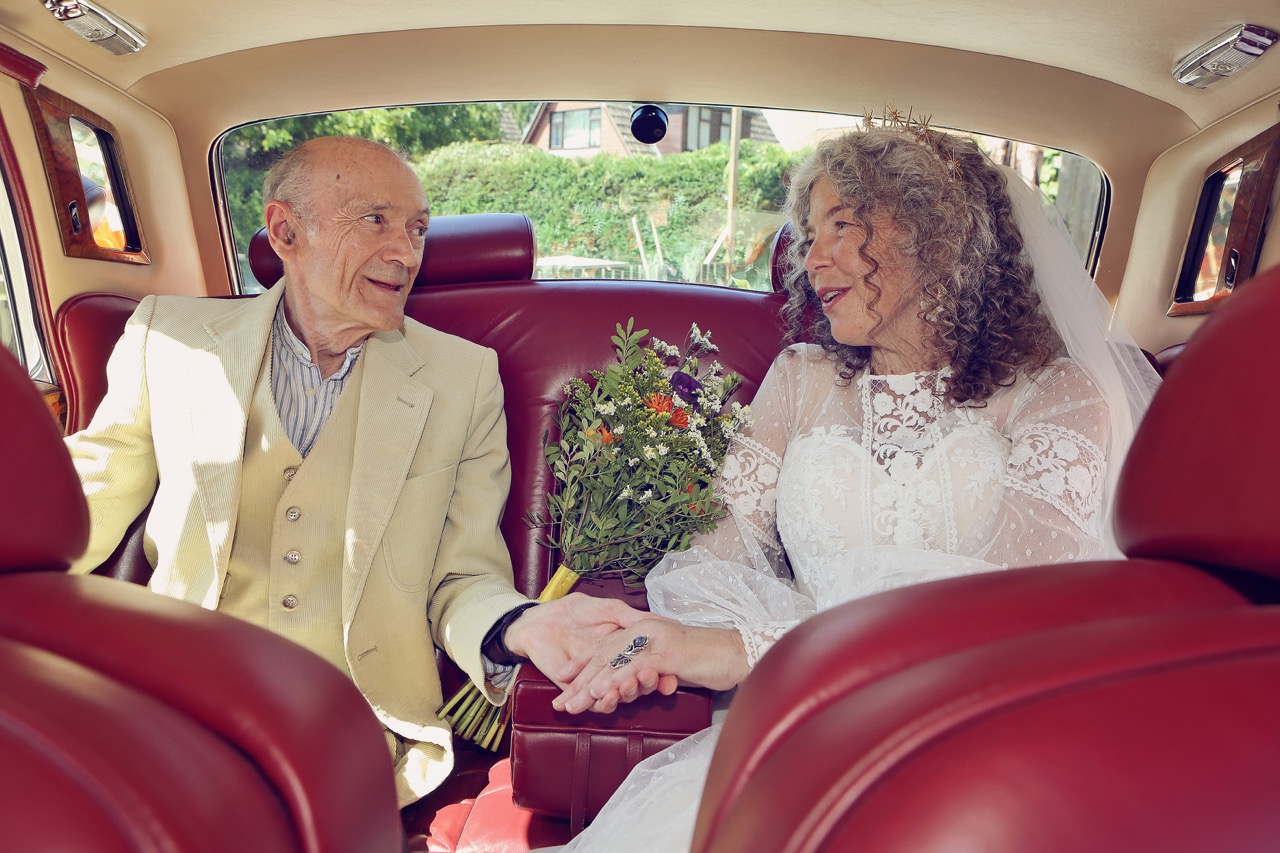 mature bride and groom sitting in retro car and holidng hands