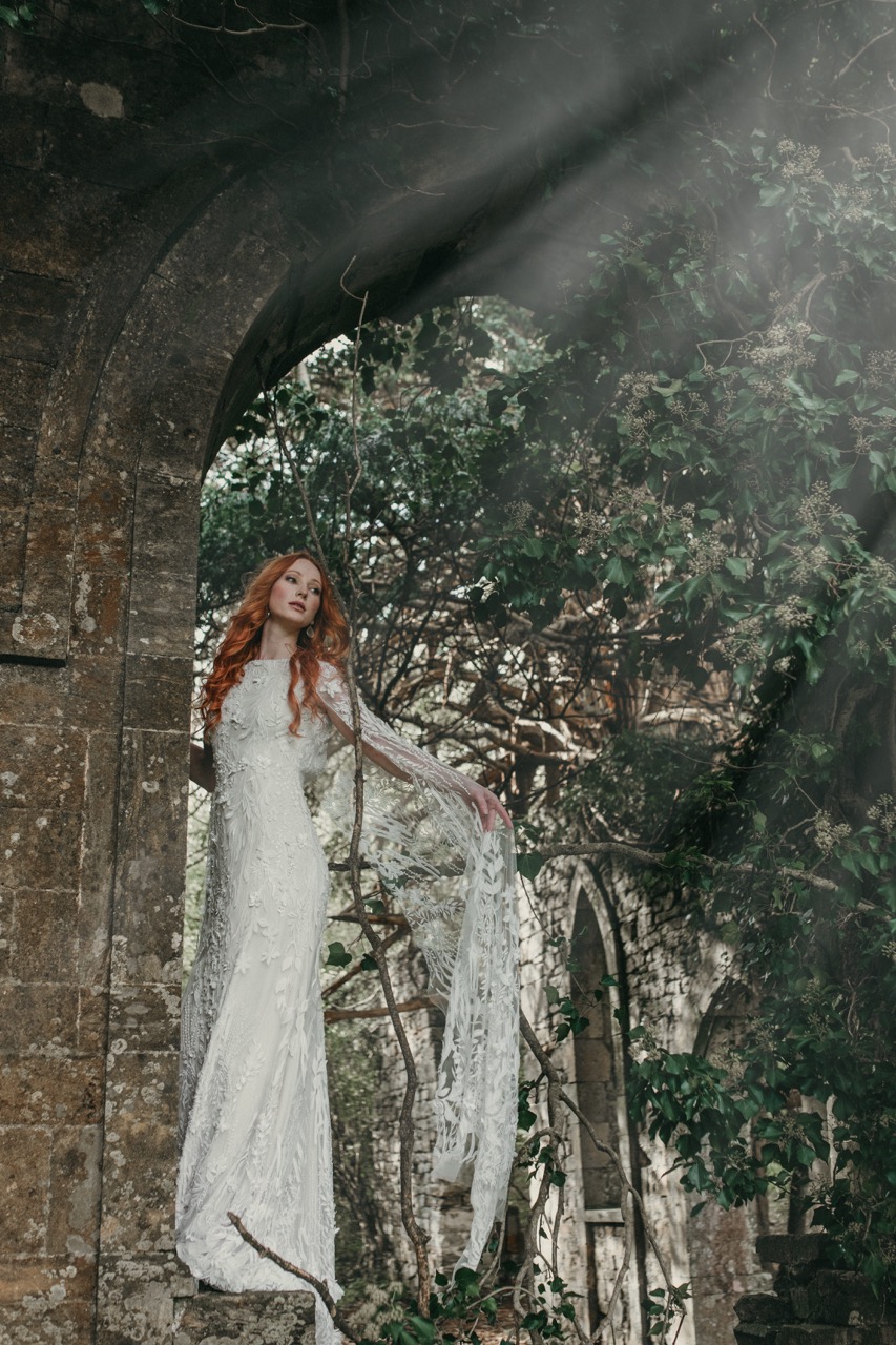 bride standing in an archway wearing an ethereal wedding dress with cape