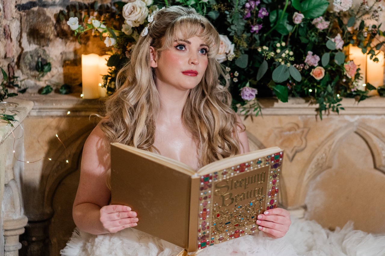bride with long blonde hair reading a 'sleeping beauty' book on disney themed wedding day