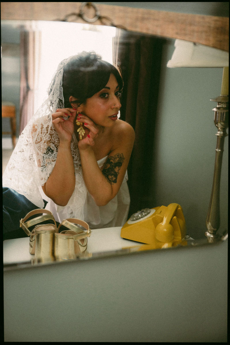 Bride with Retro hair and makeup putting on her earrings in the mirror