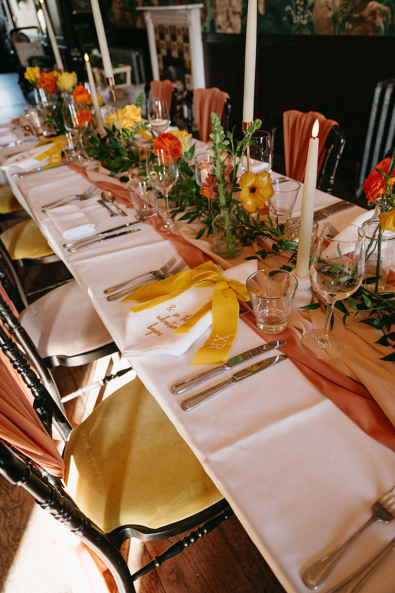 Alternative table styling with embroidered napkins, orange and yellow florals, orange runner for 1970s retro wedding