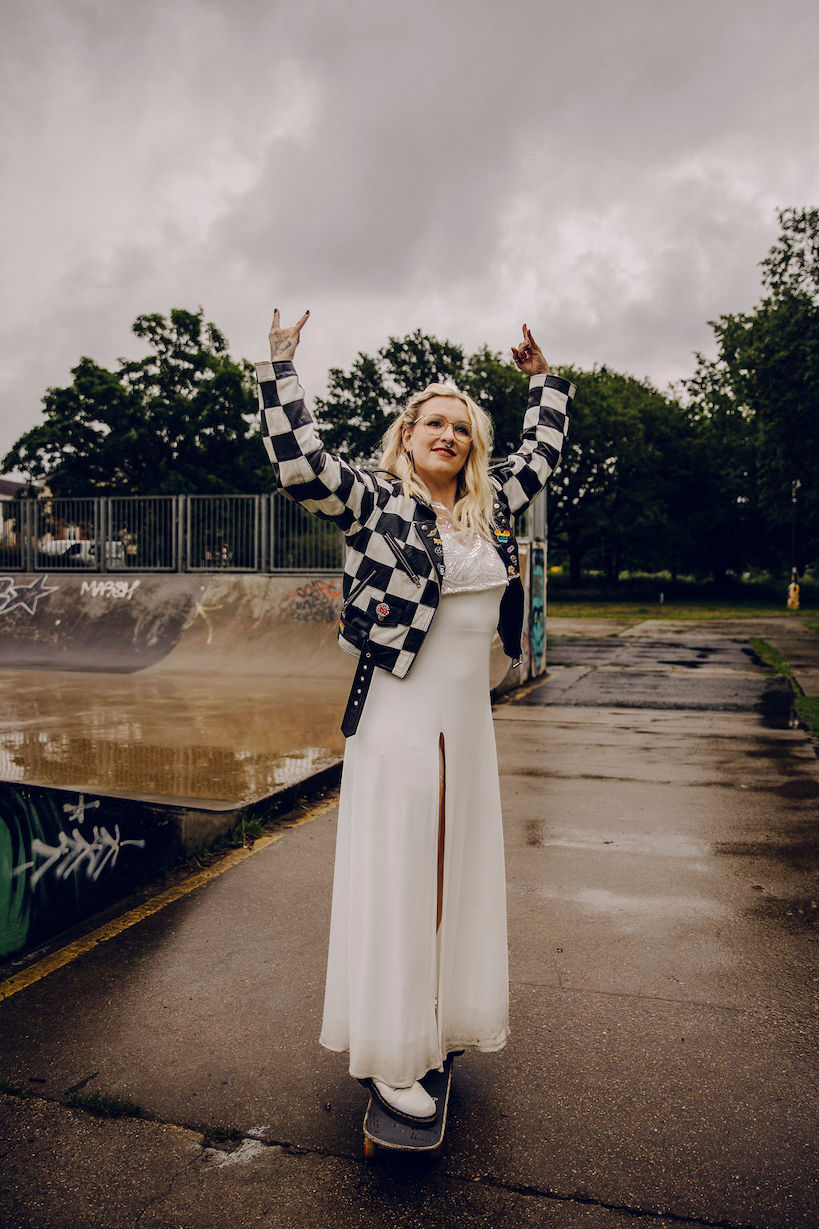 Emo bride on a skateboard at a skate park wearing wedding dress and checkerboard jacket