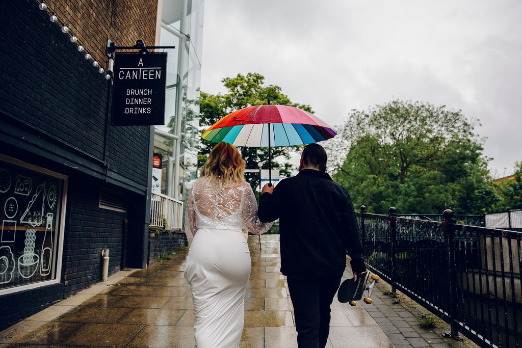Bride and groom walking through the city with a rainbow umbrella