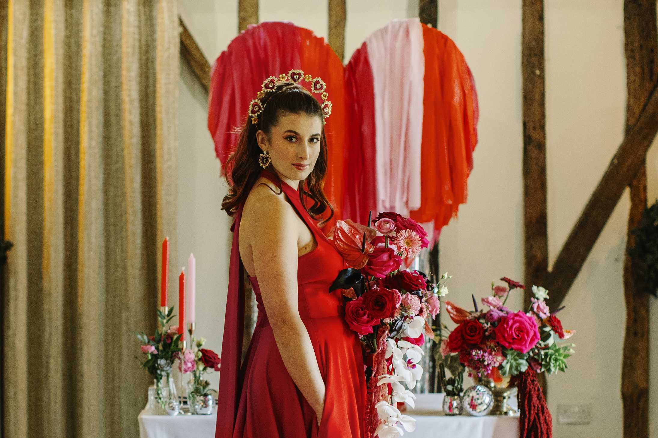 Pink and red love heart backdrop with pink and red florals. Bride wearing pink and red wedding dress and heart crown and earrings