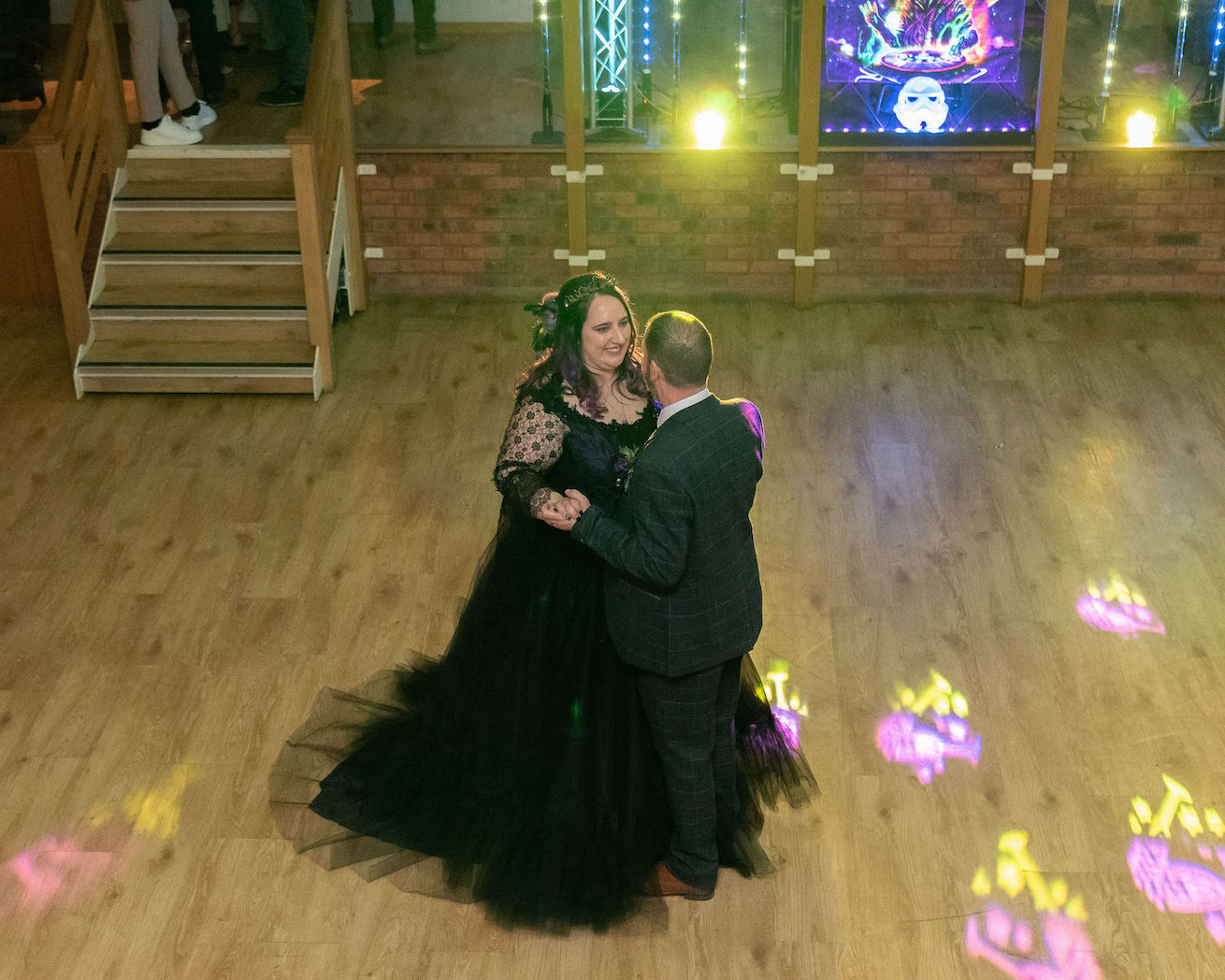 Bride and groom on hte dance floor having their first dance. The bride wears a black wedding dress and the groom a navy suit
