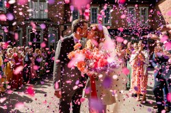 bride and groom just married. the stand outside their leeds wedding venue sharing a kiss whilsts guests watch on and throw lots of pink coloured confetti
