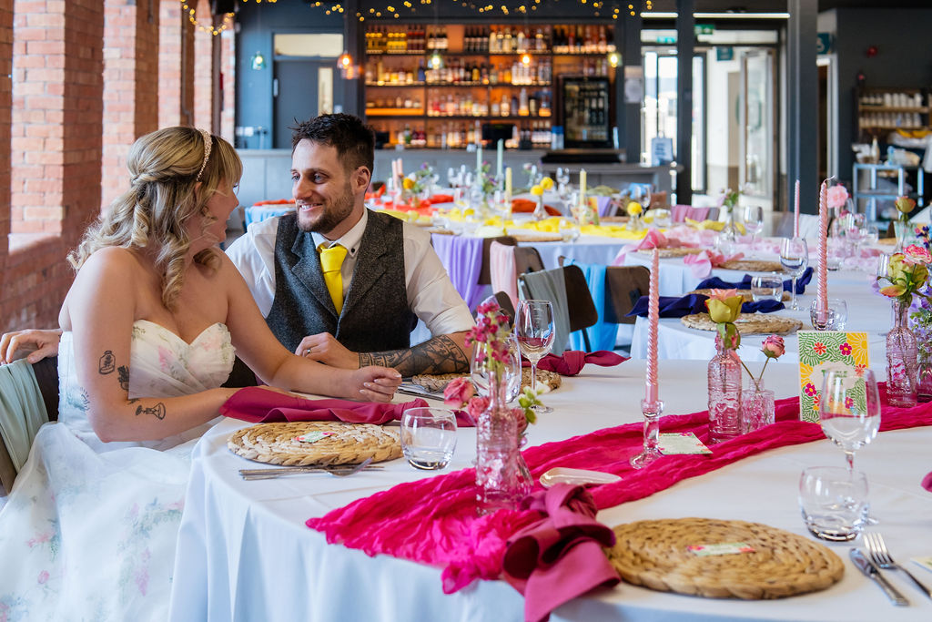 couple sit at the wedding breakfast table which is decorated all in bright pink as part of a table caterpillar